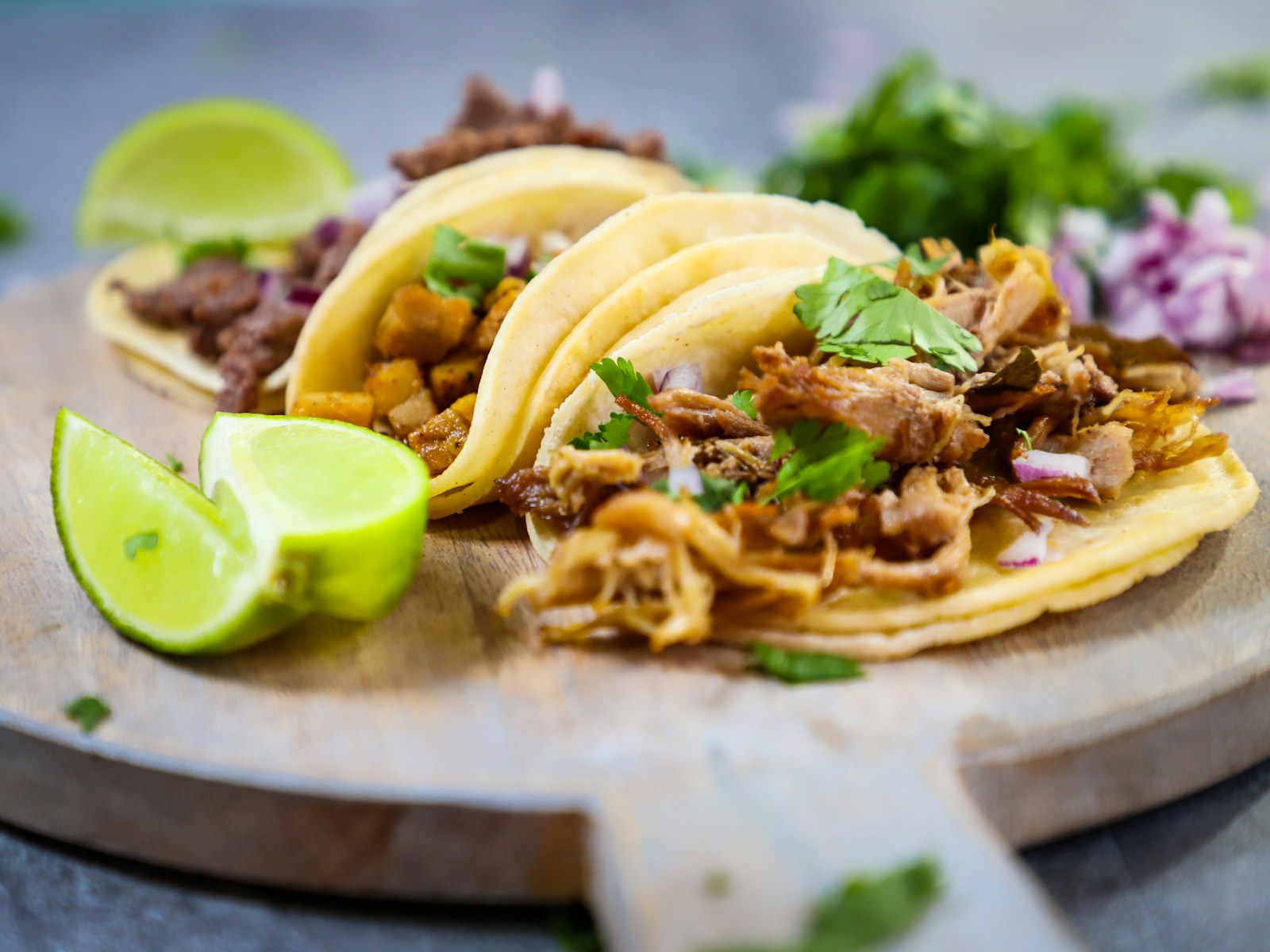 Tres tacos con cilantro, cebolla y limón sobre una tabla de madera